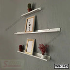 Modern white wall shelves mounted on a gray wall, displaying frames, small plants, and decor.