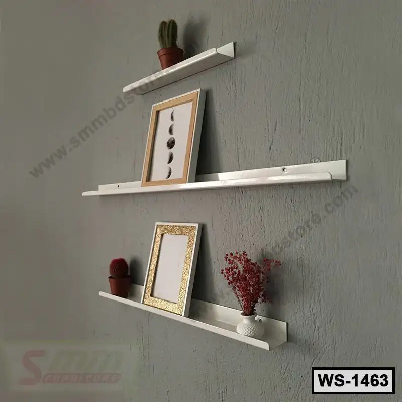 Modern white wall shelves mounted on a gray wall, displaying frames, small plants, and decor.