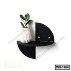 Modern black wall shelf with geometric design, holding a white vase with green plant.