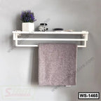 Wall-mounted white shelf with towel bar, holding decor, jar, brush, and folded towel