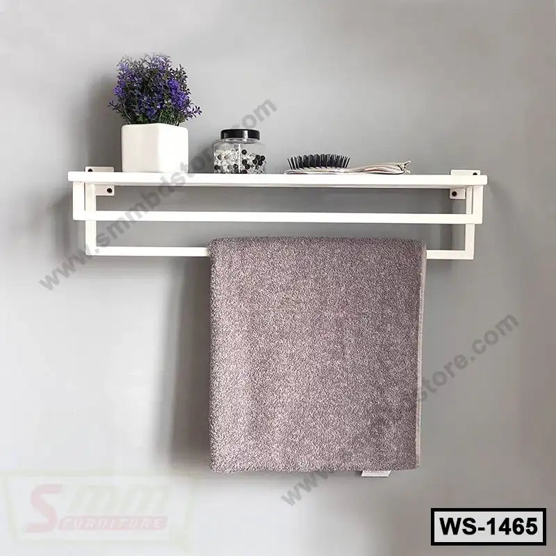 Wall-mounted white shelf with towel bar, holding decor, jar, brush, and folded towel