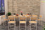 Modern wooden dining table with six chairs, set for a meal, against a stone accent wall