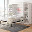 Modern wall bed with white shelves in a bright bedroom, city view window, and cozy bedding.
